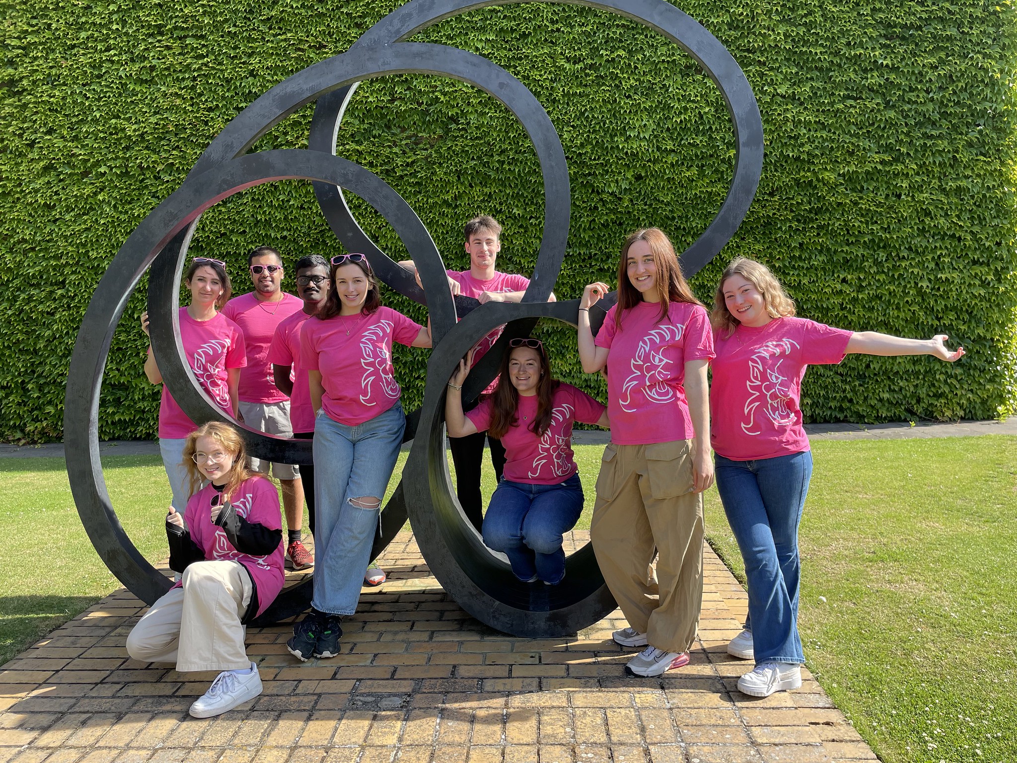 A group of students wearing pink t-shirts standing by a sculpture