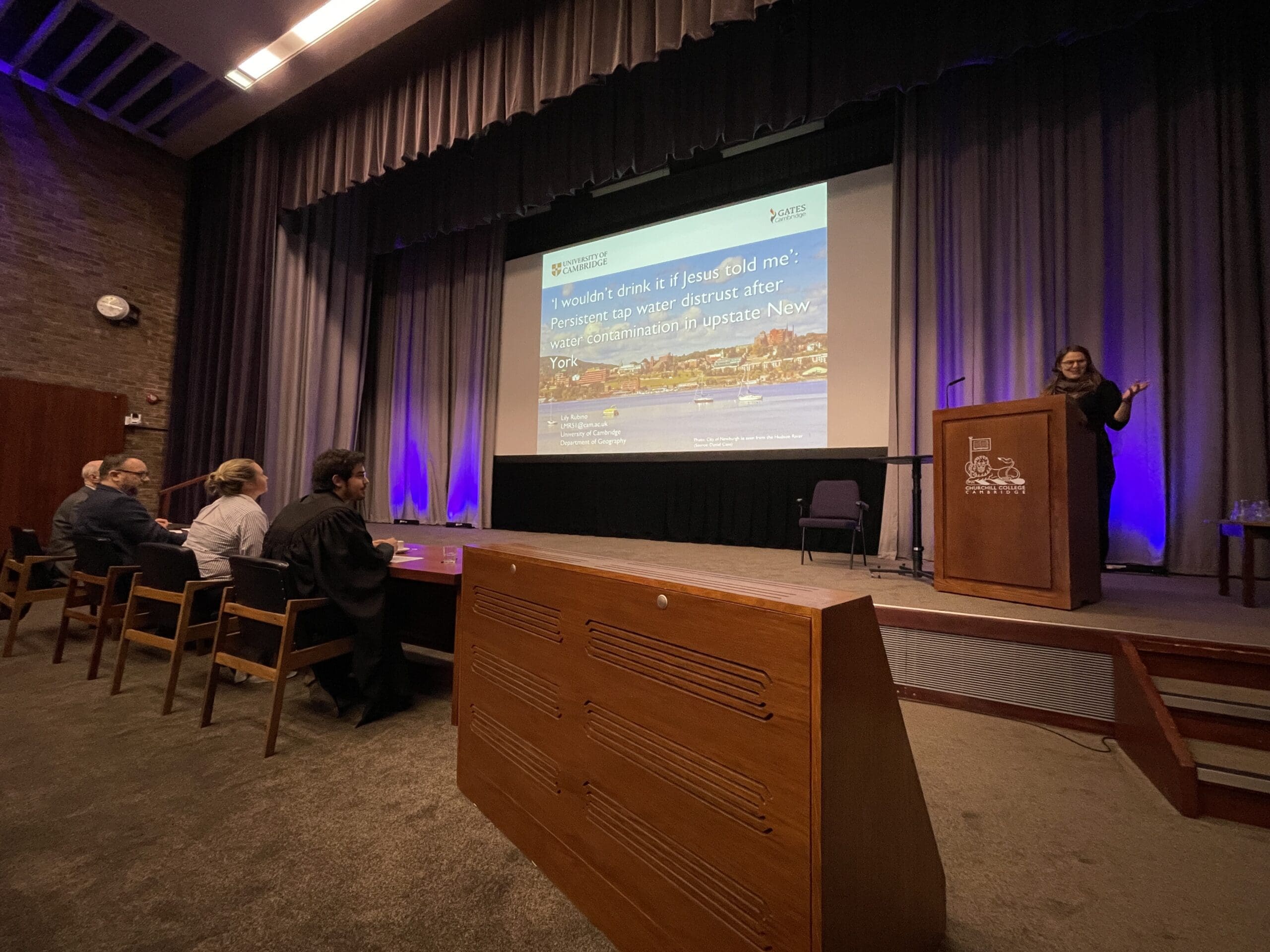 A woman presenting on stage in the Wolfson Hall