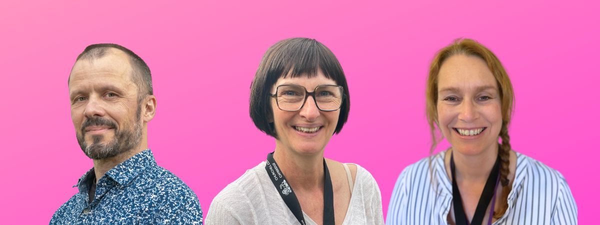 Three people are standing in front of a vibrant pink background. The first person on the left has a beard and is wearing a patterned blue shirt. The middle person has glasses and short hair. The person on the right has long hair and is wearing a striped shirt.