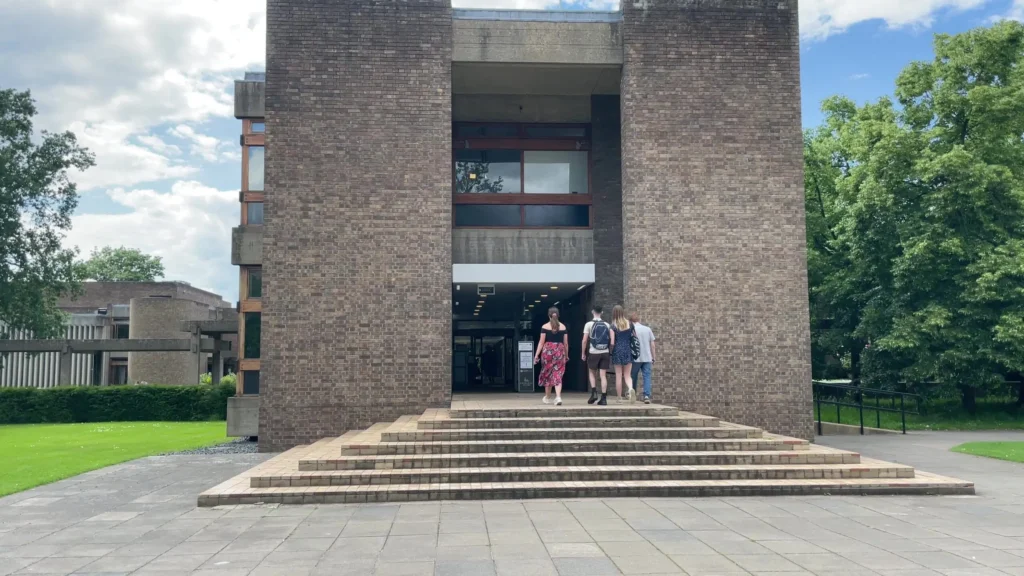 Students entering Churchill College, a modernist building with three young people walking up the steps