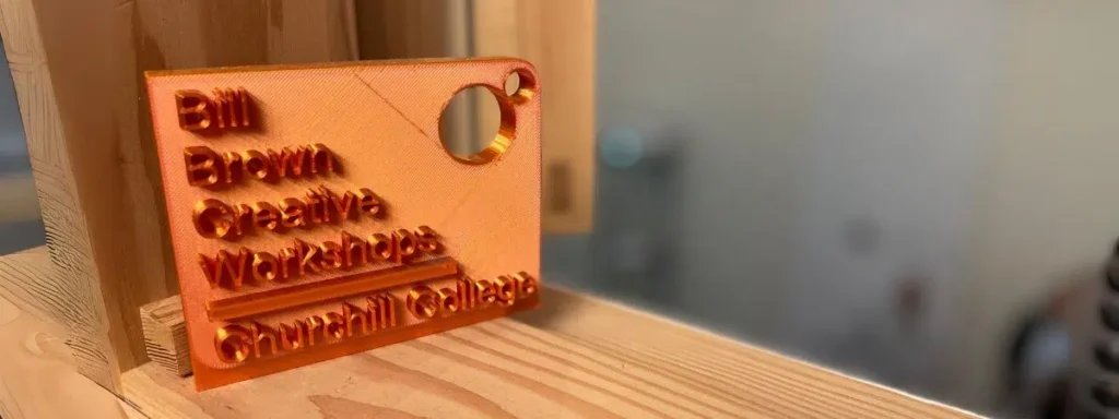 An orange plastic 3D printed keyring reading "Bill Brown Creative Workshop"