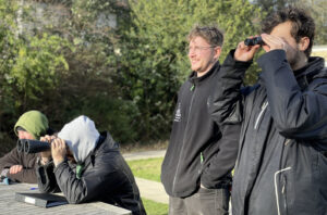 Three men birdwatching through binoculars, focused and engaged in their exploration.